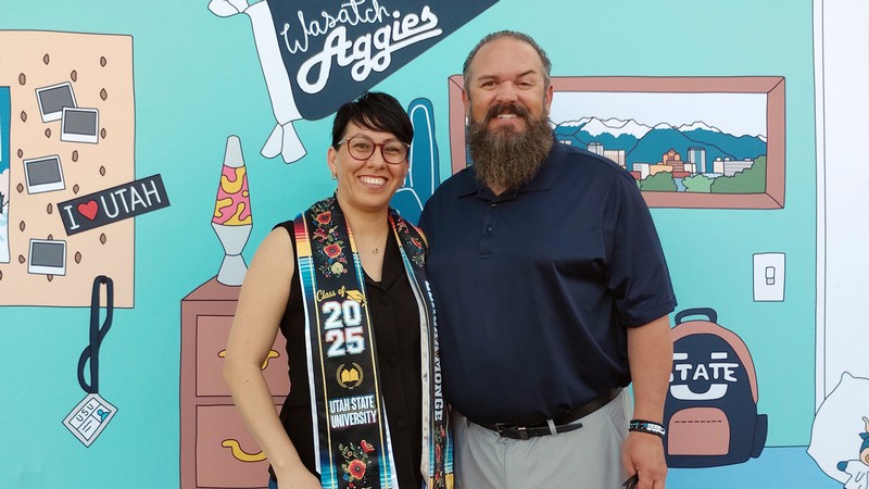 A man and a woman pose in front of a graduation background.